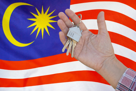 Hand shows the keys to the apartment on background of flag Malaysia. Keys to the apartment in a female hand on background of flag Malaysia. Realty concept and home buying or new apartment in Malaysiaの写真素材