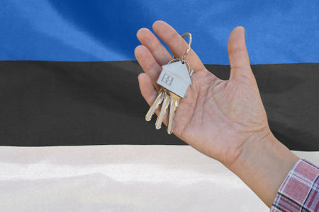 Hand shows the keys to the apartment on background of flag Estonia. Keys to the apartment in a female hand on background of flag Estonia. Realty concept and home buying or new apartment in Estoniaの写真素材