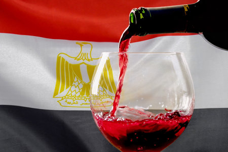 Red wine pouring from a bottle into a glass against the background of the Egyptian flag. Concept of winemaking and wine export in Egyptの写真素材