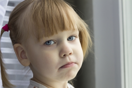 Distraught girl standing near the window  の写真素材