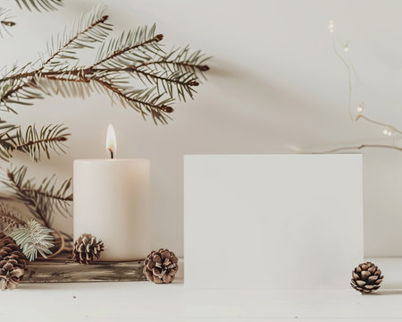 Cozy winter arrangement with a postcard, candles, and pine cones on a neutral background, copyspace.の写真素材