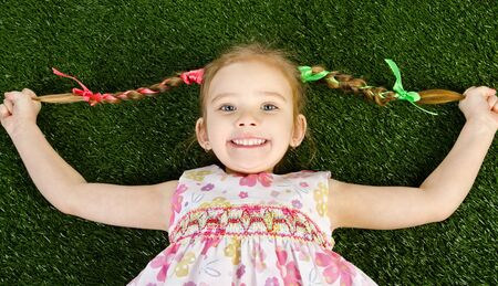 Smililing happy little girl lying on grass and  holding her braids