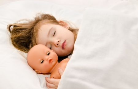 Adorable little girl sleeping in the bed with her dollの写真素材