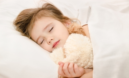 Adorable little girl sleeping in the bed with her toy の写真素材