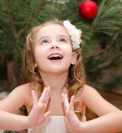 Happy adorable little girl near christmas tree looking upの写真素材