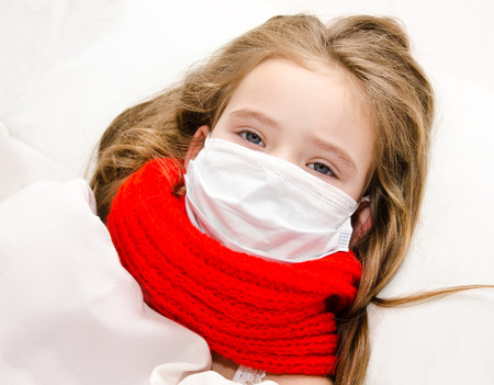 Sick little girl with surgical face mask for bacterial and virus flu protection and scarf in the bedの写真素材