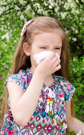 Little girl has allergy to spring blossoming and blowing her nose outdoorの写真素材