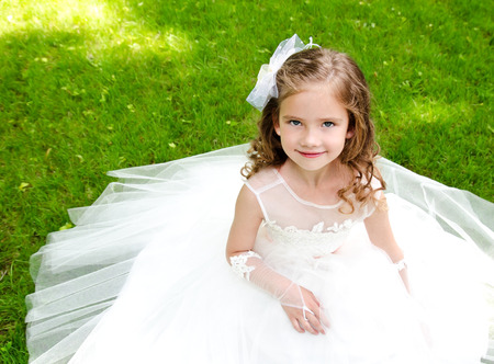 Adorable smiling little girl in princess dress sitting on grass outdoorの写真素材