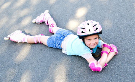 Cute smiling little girl in pink roller skates and protective gear outdoor