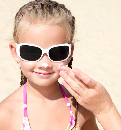 Mother anoints protective cream to face  little girl child on the beach