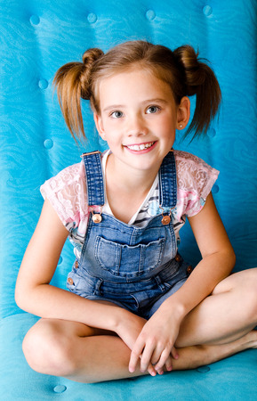 Portrait of adorable smiling little girl child sitting on the sofaの写真素材