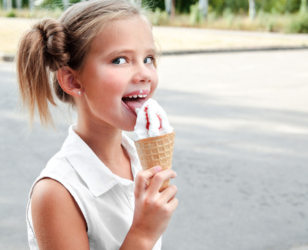 Cute smiling little girl eating an ice cream outdoorの写真素材