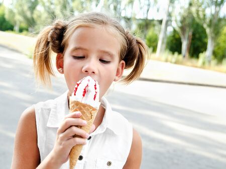 Cute smiling little girl eating an ice cream outdoor