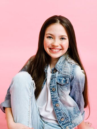Portrait of adorable smiling little girl child in jeans isolated on a pink background