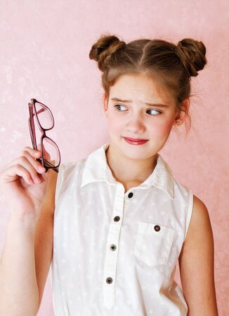 Disappointed dissatisfied little girl child preteen holding eyeglasses education, school and vision concept isolated on a pinkの写真素材