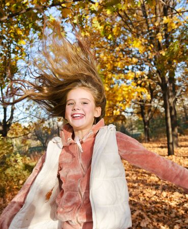 Autumn portrait of adorable smiling little girl child preteen having fun and jumping  in the park outdoorsの写真素材