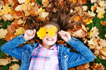 Autumn portrait of adorable smiling little girl child preteen lying in leaves in the park outdoorsの写真素材