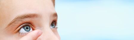 Little girl child putting contact lens into her eye isolated on blueの写真素材