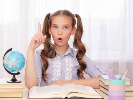 Education and school concept. Child is sitting at the desk with finger up and say Ooo. Cute little...