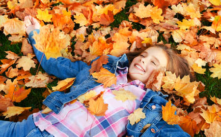 Autumn portrait of happy smiling little girl child lying in leaves in the park outdoors