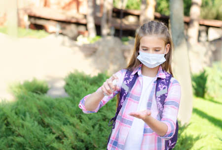 Little girl child with face mask and sanitizer. Education concept. Back to school after covid-19. Preteen student disinfecting hands after school outdoors.の写真素材