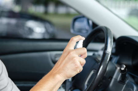 Man sanitizing wheel and salon of his car. Male hand holding sanitizer closeup. Disinfection hygiene...