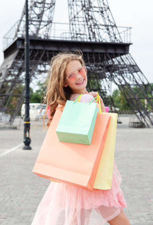 Beautiful happy smiling little girl child in sunglasses are holding shopping bags outdoors and Eiffel Tower in background .. Lifestyle conceptの写真素材