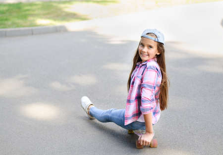 Smiling cute little girl child sitting with a skateboard. Preteen with penny board outdoors in summer dayの写真素材