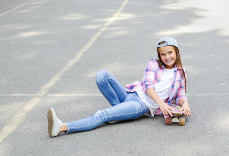 Smiling happy cute little girl child skating on a skateboard. Preteen riding on a penny board outdoors in summer dayの写真素材