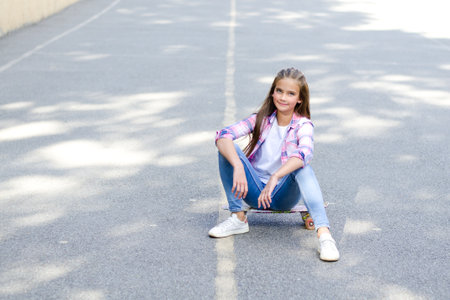 Smiling cute little girl child sitting with a skateboard. Preteen with penny board outdoors in summer dayの写真素材