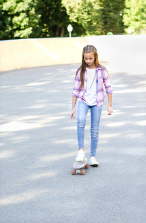 Smiling cute little girl child sitting with a skateboard. Preteen with penny board outdoors in summer dayの写真素材