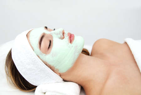 Beautiful young woman with facial mask in beauty salon. Girl getting beauty treatment facial careの写真素材