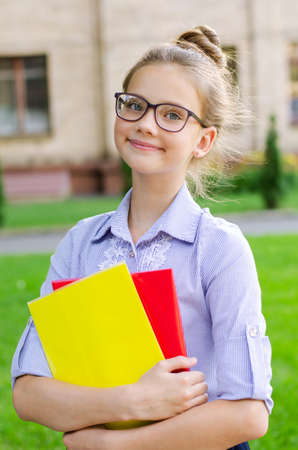 Back to school. Education concept. Cute smiling schoolgirl in glasses outdoor. Happy little girl child holding the booksの写真素材