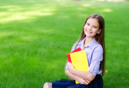 Back to school. Education concept. Cute smiling schoolgirl sitting on grass. Happy little girl child holding the booksの写真素材