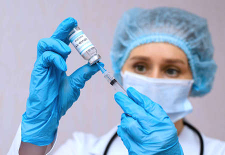 Doctor, nurse, scientist hand in blue gloves holding coronavirus, covid-19 vaccine and syringe.の写真素材