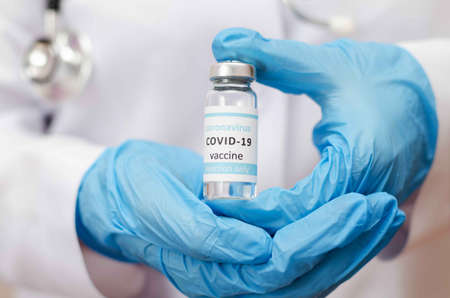 Doctor or laborant in protective gloves holding ampule tube with nCoV Coronavirus vaccine for COVID...