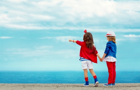 Fashion kids stands on stone breakwater and points to the sea  Vacation, friendship, fashionable concept の写真素材