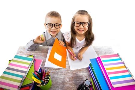 Two smiling little kids at the table children doing homework, isolated on white background  School,...