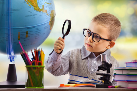 Boy looking through magnifying glass at globe, isolated on white background. School, education concept.の写真素材