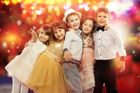 Group of happy kids in celebratory clothes with colorful lights on background. Holidays, christmas, new year, x-mas concept.