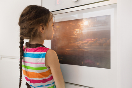 Little girl waiting near the kitchen oven for the homemade cookies. Baking. Children cooking conceptの写真素材