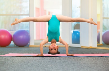 Flexible little girl gymnast standing on head in gym. Sport, training, fitness, yoga, active lifestyle conceptの写真素材
