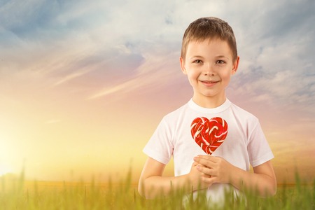 Little boy with candy red lollipop in heart shape on nature backgroundの写真素材