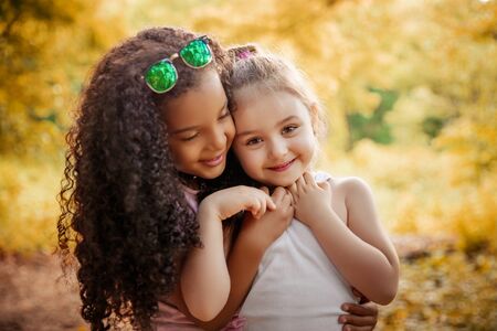 Two happy girls as friends hug each other in cheerful way. Little girlfriends in park.の写真素材