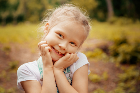 Adorable smiling little blonde girl with braided hair. Cute child having fun on a sunny summer day outdoor. Sun light. Glow sun. Happy day. Warm photo. Outdoor portrait.の写真素材