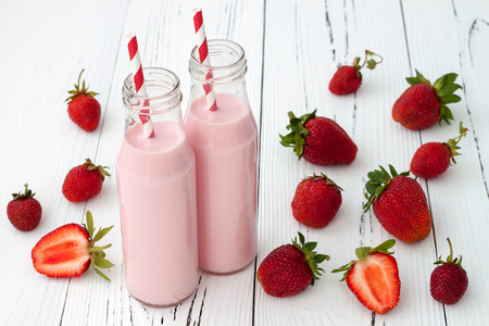 Strawberry milk in traditional glass bottles with straws on old vintage wooden backgroundの写真素材
