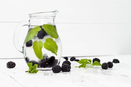 Healthy detox water with blackberry and mint. Cold refreshing berry drink with ice on white wooden table. Copy space backgroundの写真素材