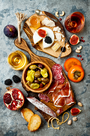 Appetizers table with italian antipasti snacks and wine in glasses. Brushetta or authentic traditional spanish tapas set, cheese variety board over grey concrete background. Top view, flat layの写真素材