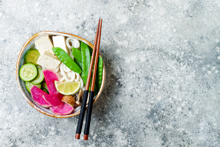 Vegan asian udon noodles soup bowl with ginger and mushrooms broth, tofu, snap peas, zucchini, watermelon radish and lime.の写真素材