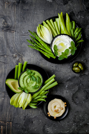 Green vegetables snack board with various dips. Yogurt sauce or labneh, hummus, herb hummus or pesto with fresh vegetables. Healthy raw summer platter.の写真素材